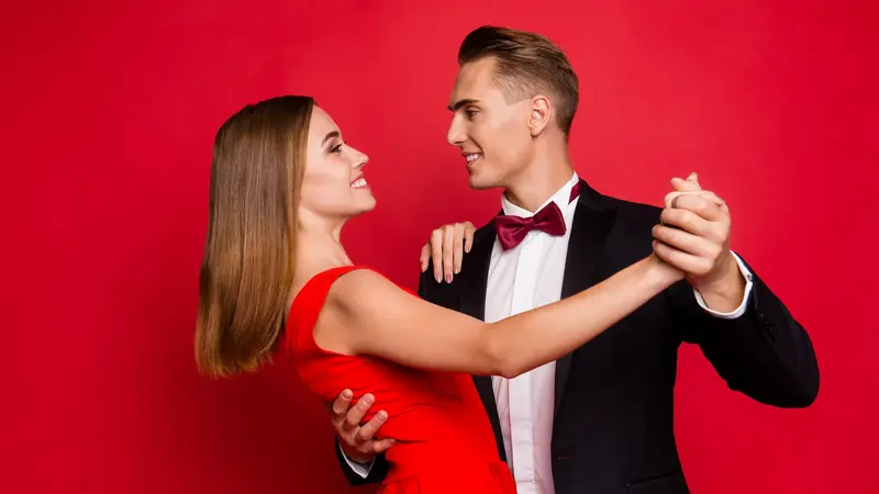 Tanzendes Paar in festlicher Kleidung vor rotem Hintergrund.