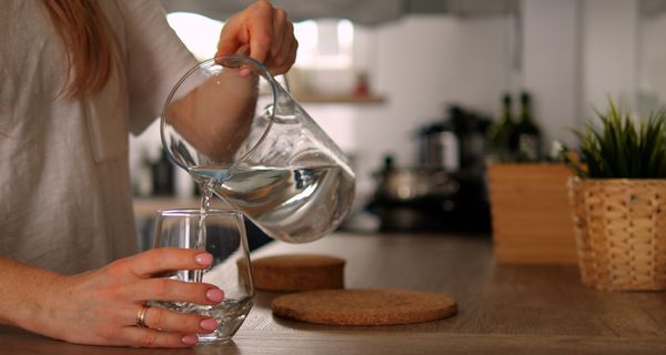 Frau, schenkt sich Wasser in ein Glas ein.