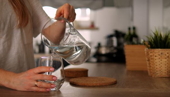 Frau, schenkt sich Wasser in ein Glas ein.