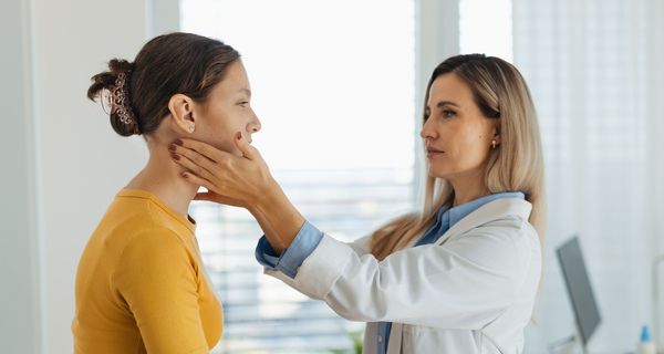 Ärztin tastet die Halslymphknoten bei einer Patientin ab.