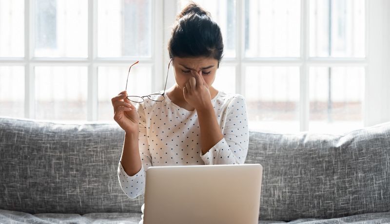 Junge Frau, sitzt vor dem Laptop und reibt sich die Augen.