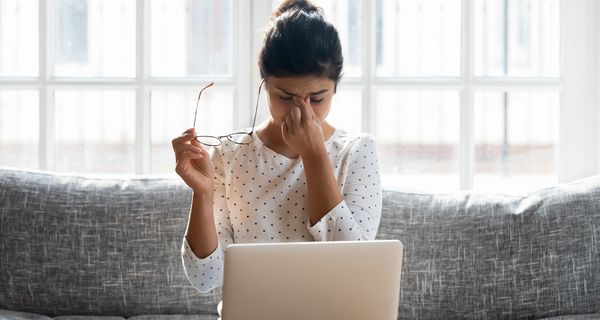 Junge Frau, sitzt vor dem Laptop und reibt sich die Augen.