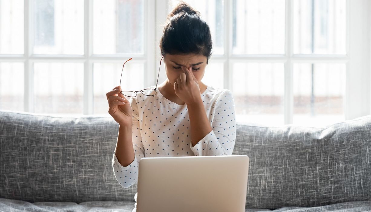 Junge Frau, sitzt vor dem Laptop und reibt sich die Augen.