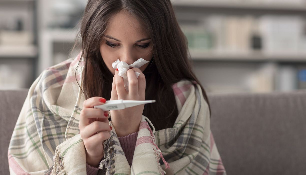 Junge Frau mit Taschentuch und Fieberthermometer.