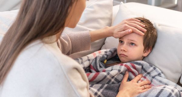 Junge, hat Fieber und liegt mit einer Decke auf einer Couch.