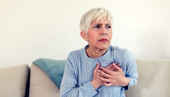 Frau sitzt auf den Sofa und hält die Hände auf die Brust