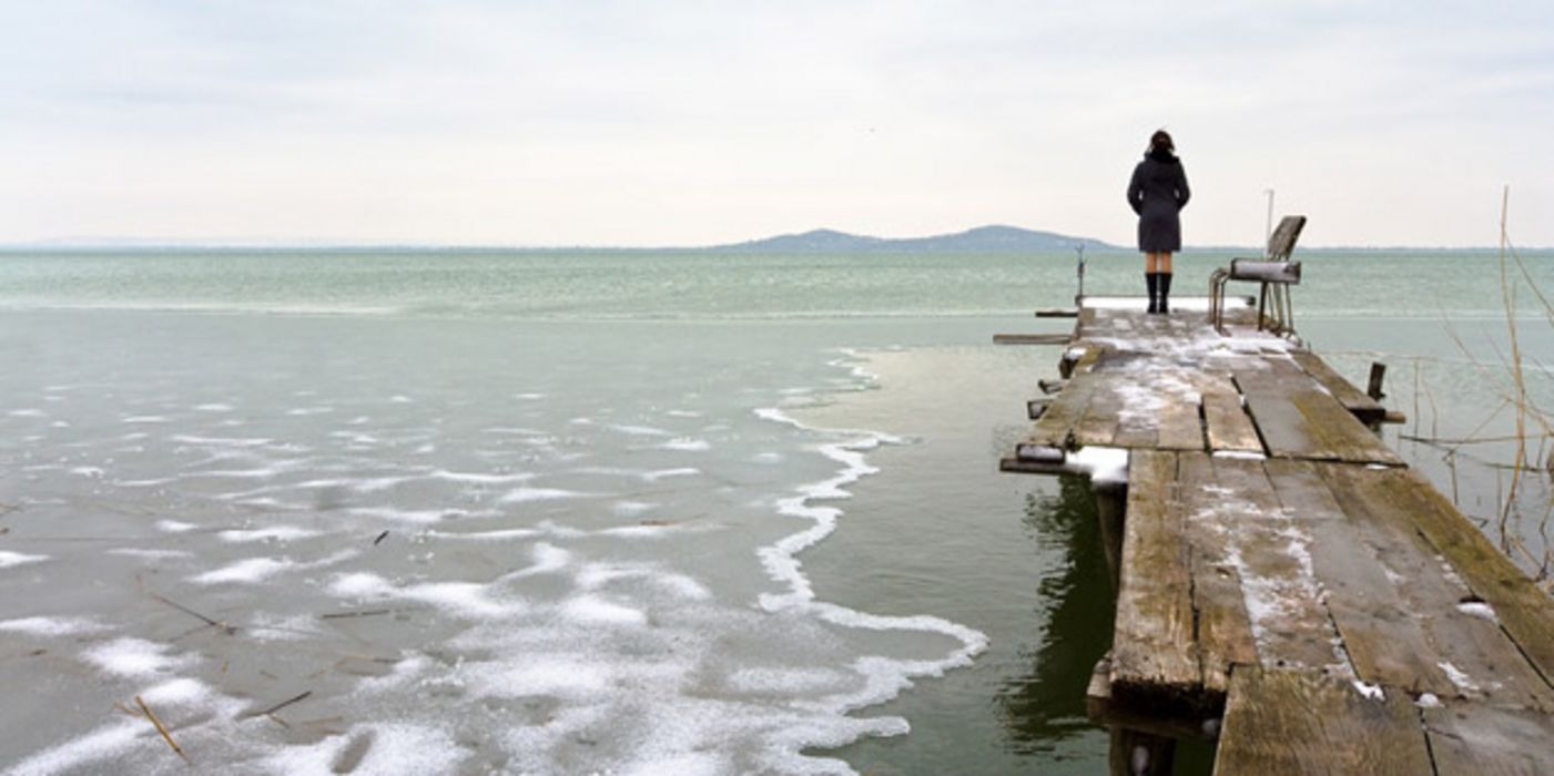 Mensch auf Steg blickt über einen See.