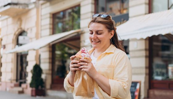 Frau kommt mit Törtchen in der Hand aus einer Konditorei.
