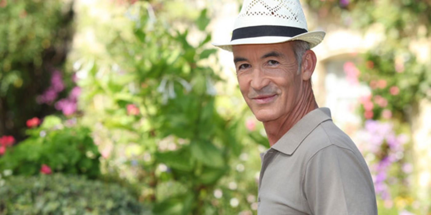 Mann mit Strohhut und Polo-Shirt draußen im Schatten