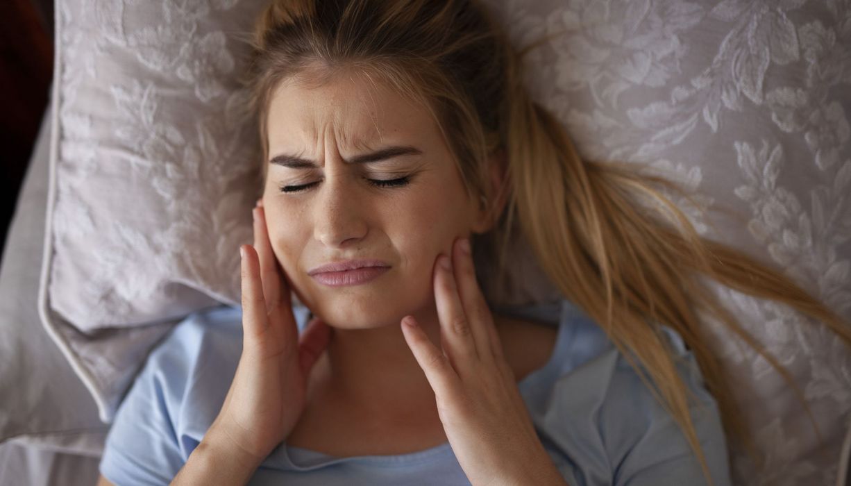 Frau mit Kieferschmerzen, liegt im Bett.