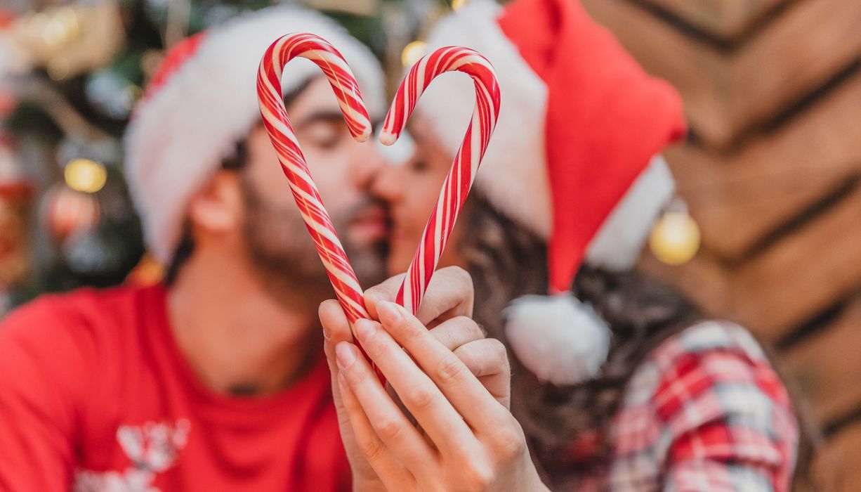 Junges Liebespaar küsst sich und hält Zuckerstangen in die Luft.