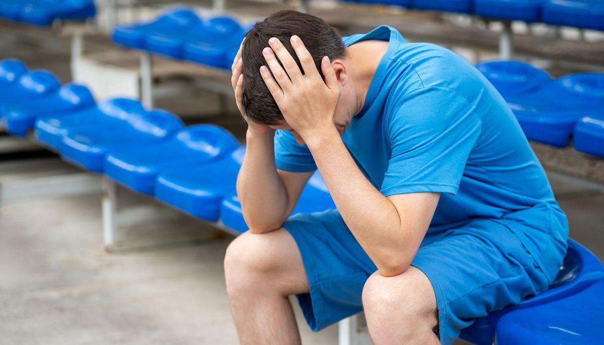 Mann, sitzt in einem Sportstadion und hält sich den Kopf.