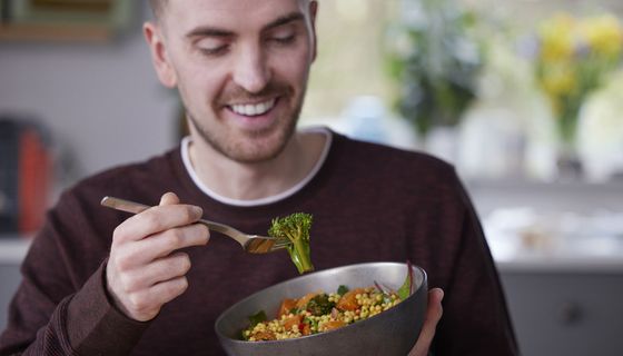 Mann isst ein veganes Gericht mit Samen, Brokkoli und Tomaten.