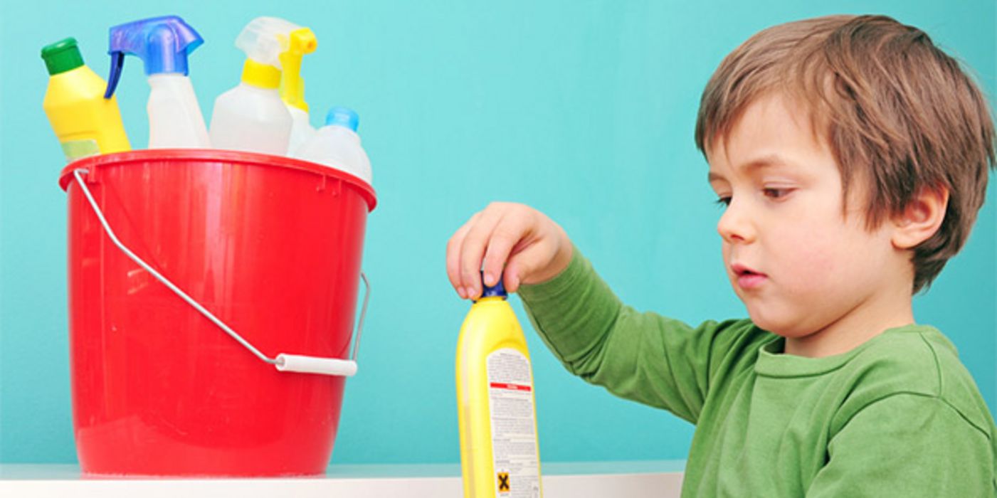 Junge, ca. 3 Jahre, roter Putzeimer mit Putzmitteln, gelbe Flasche in der Hand, versucht sie aufzumachen