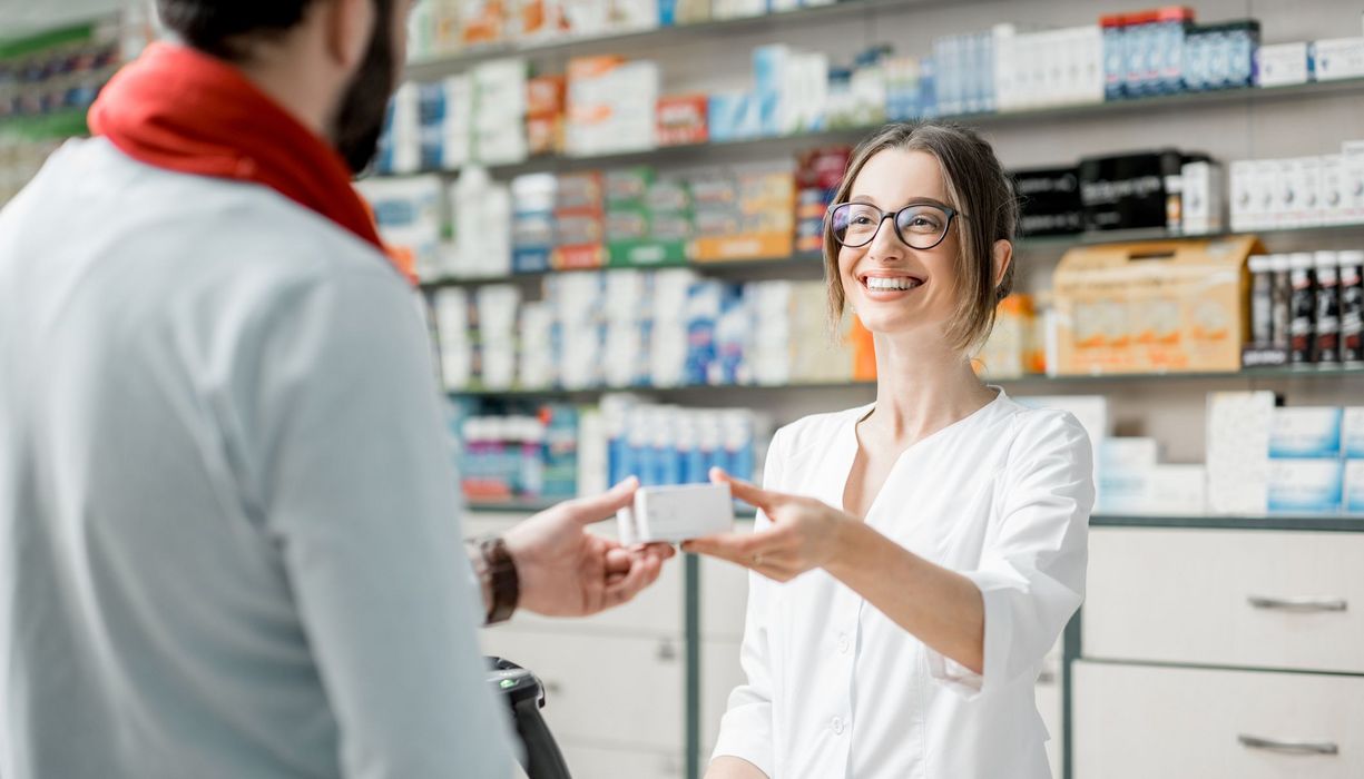 Junge Apothekerin, reicht ein Medikament über die Theke.