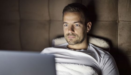 Ein Mann sitzt aufrecht im Bild und schaut auf sein Laptop.
