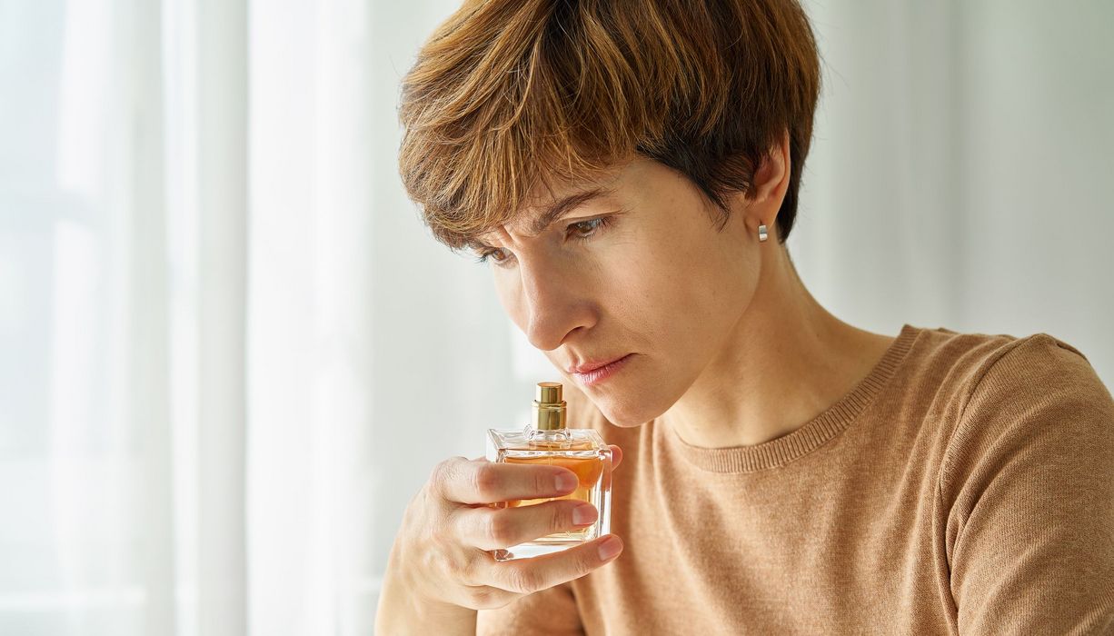 Frau, riecht an einem Fläschchen Parfum.