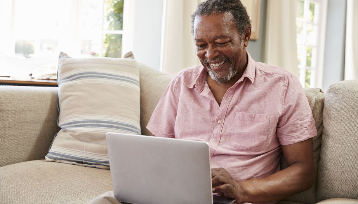 Älterer Mann, sitzt mit einem Laptop auf der Couch.