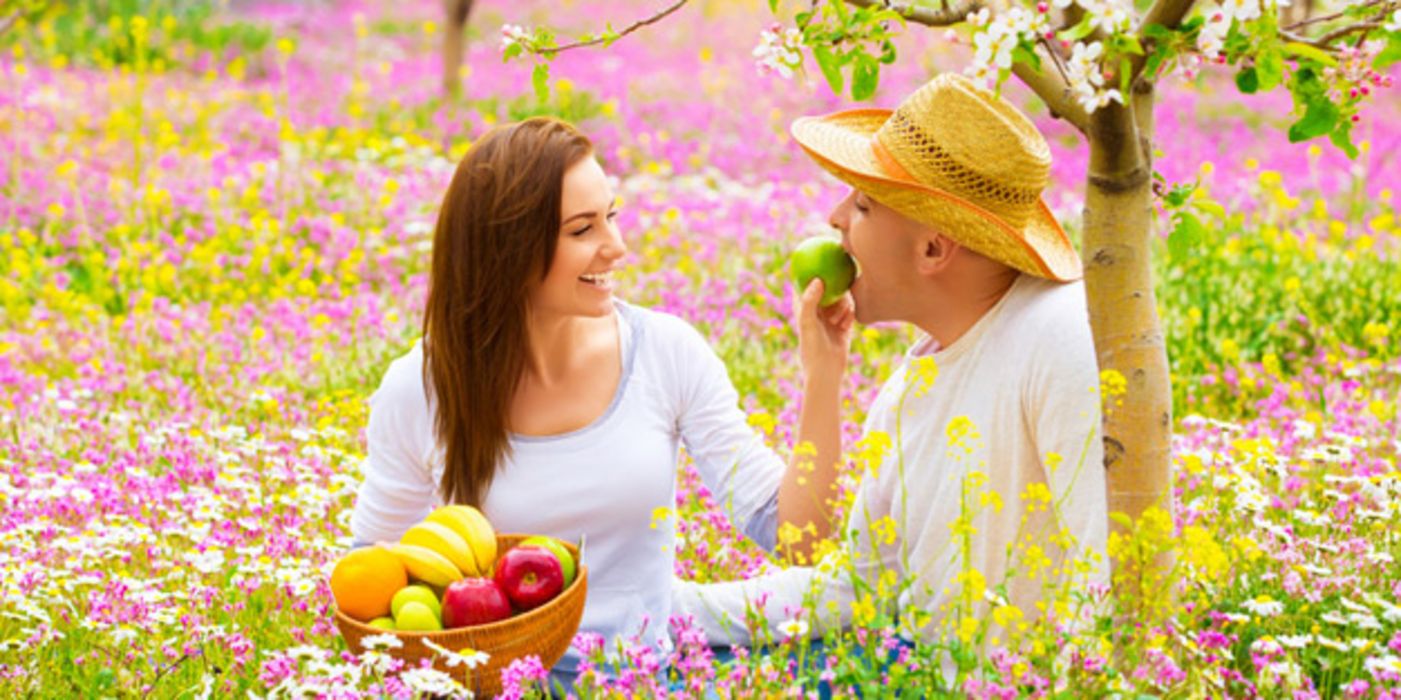 Junges Paar isst Obst auf Blumenwiese.