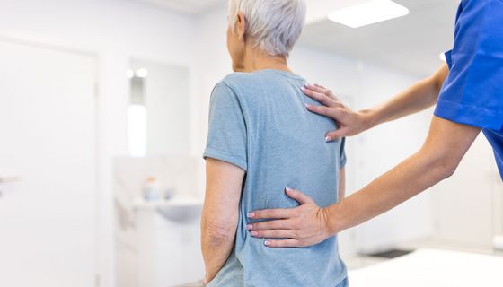 Frau legt Hände auf Rücken einer sitzenden Frau
