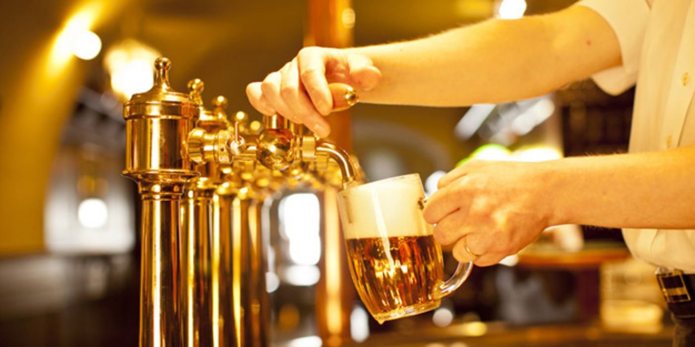 Bierzapfanlage in Kneipe/Pub, Arm von rechts ins Bild ragend zapft gerade ein Bier in einen Humpen.