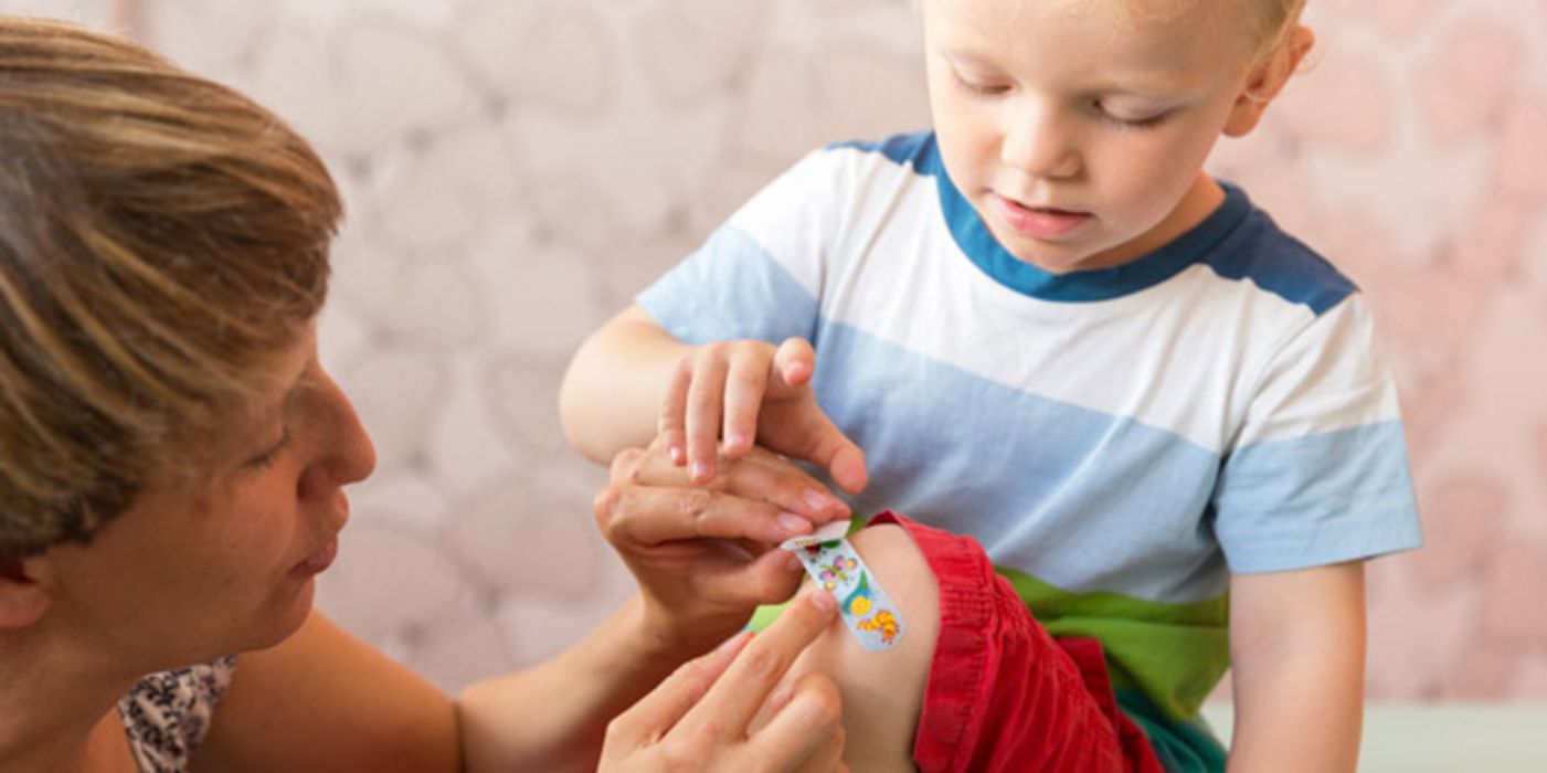 Mutter klebt kleinem Jungen ein Pflaster aus das Knie.