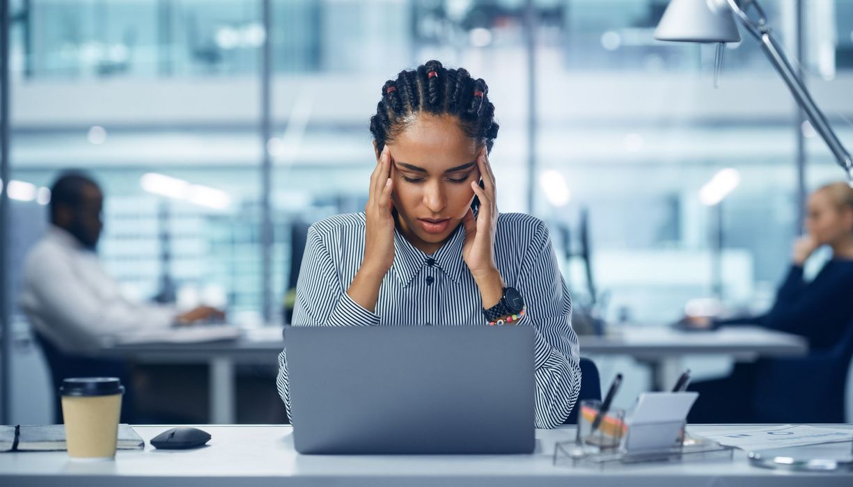 Frau, sitzt mit Migräne am Arbeitsplatz.