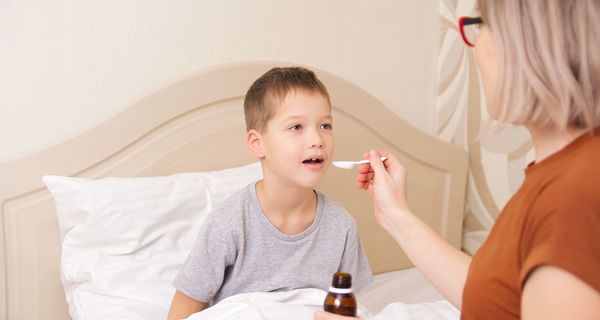 Mutter gibt Sohn Arzneimittel-Saft auf einem Löffel.