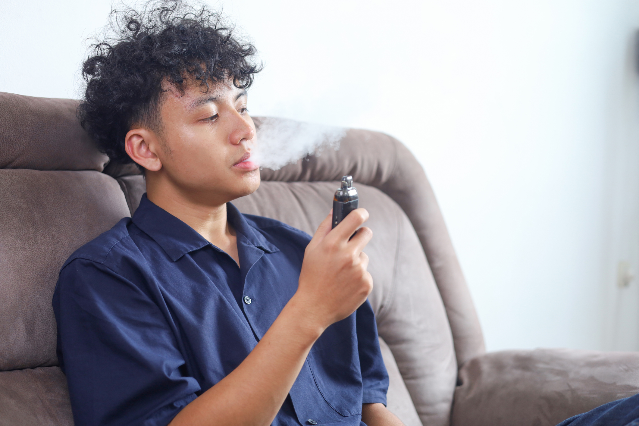 Mann dampft zu Hause auf Sofa E-Zigarette