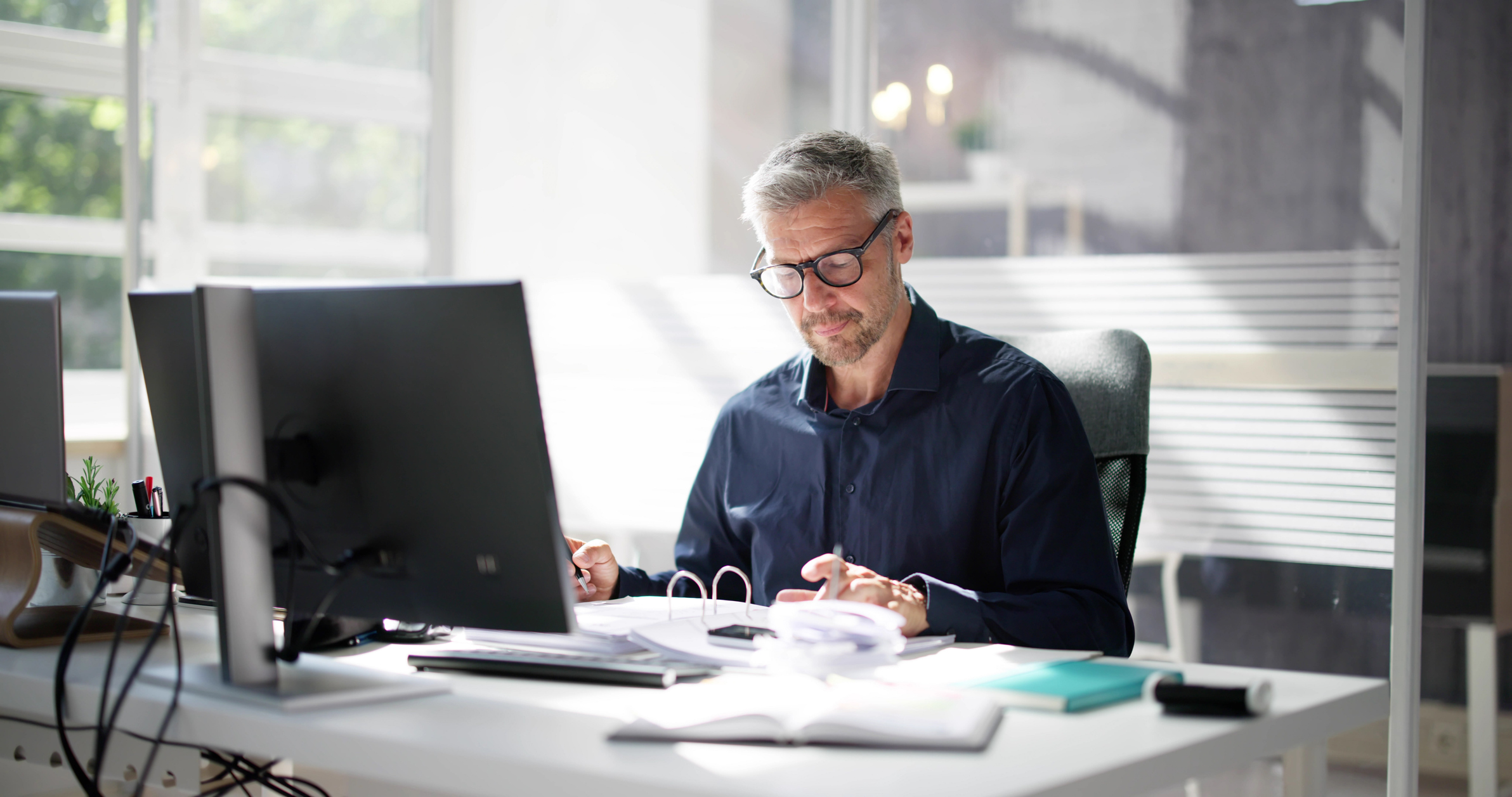 Mann sitzt im Büro am Schreibtisch und geht Dokumente durch