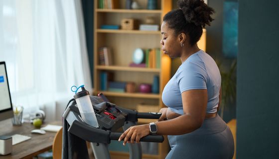 Frau auf einem Laufband zuhause. Ihr läuft ein Schweißtropfen über die Wange.