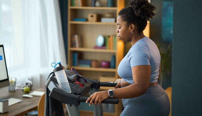 Frau auf einem Laufband zuhause. Ihr läuft ein Schweißtropfen über die Wange.
