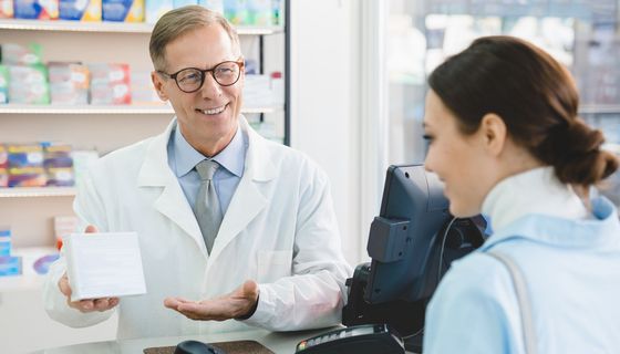 Freundlich lächelnder Apotheker überreicht einer Kundin eine große Packung mit Medikamenten.