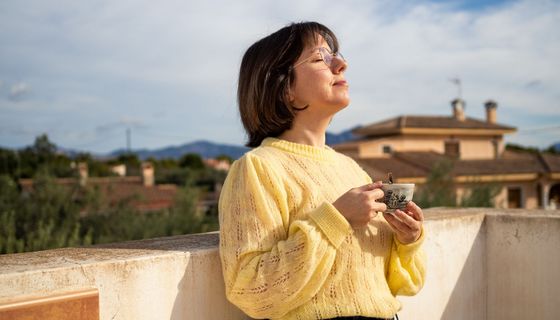 Frau, steht mit einer Tasse Kaffee auf dem Balkon.