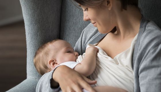 Eine Frau stillt lächelnd ihr Kind.
