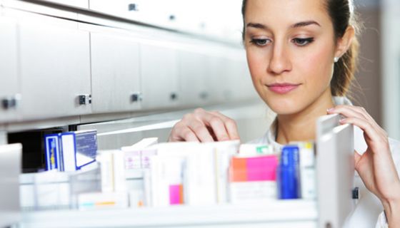 Apothekerin steht vor einem geöffneten Medikamentenschrank.