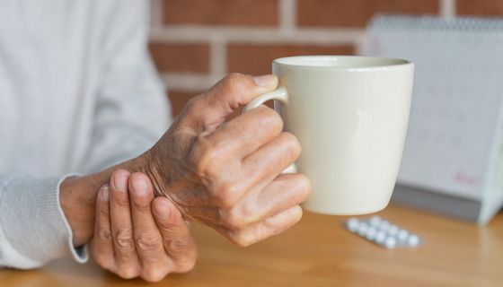 Eine ältere Person hält eine Tasse und stützt ihr Handgelenk mit der anderen Hand ab.