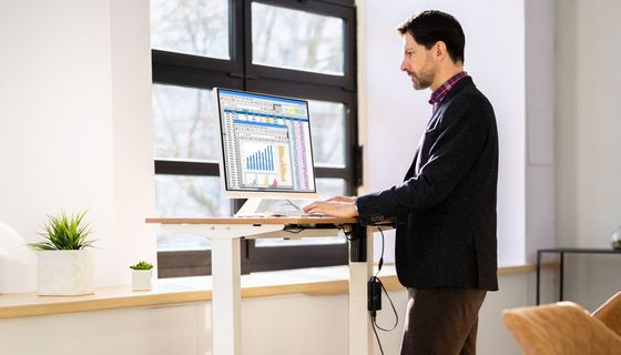 Mann arbeitet im Stehen an einem elektrisch höhen verstellbaren Tisch.