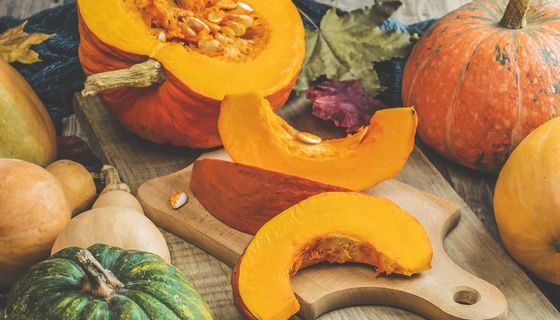 Kürbisspalten liegen auf einem Brett. Darum herum sind andere Kürbisse drapiert.