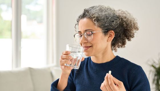 Frau über 40 nimmt eine Tablette mit einem Glas Wasser ein.