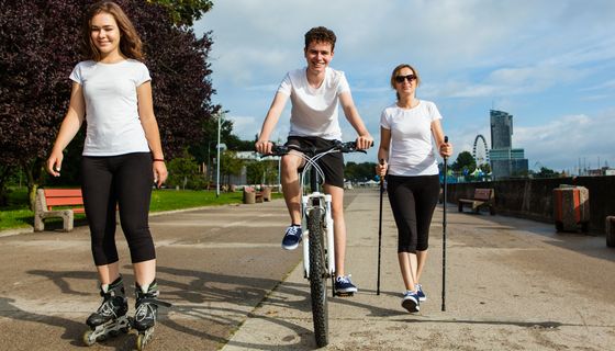 Drei junge Leute fahren Inline-Skates, fahren Fahrrad und machen Nordic Walking