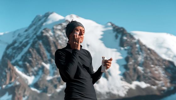 Mann steht vor Berg und cremt sein Gesicht mit Sonnencreme ein