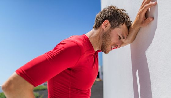 Mann lehnt schwitzend an einer Wand, er ist außer Atem.