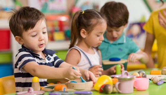 Kita-Kinder sitzen am Tisch einer Spielzeugküche.