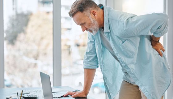 Mann mit grauem Bart hält sich den Rücken.