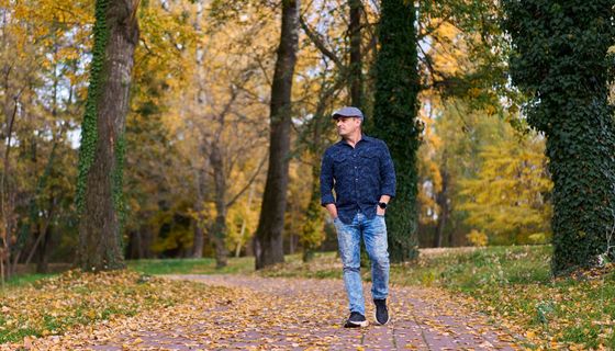 Ein Mann mit einer Schiebermütze geht im frühen Herbst durch einen Park.