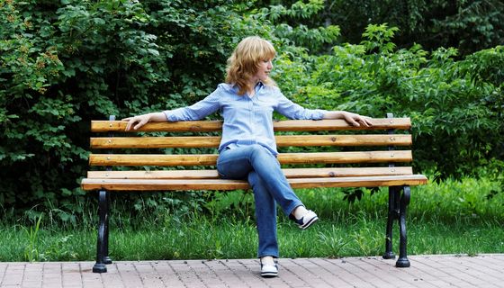 Junge Frau sitzt entspannt auf einer Bank im Grünen.