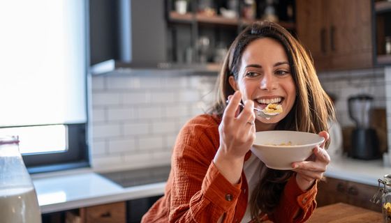 Eine junge Frau sitzt am Küchentisch und isst Müsli.