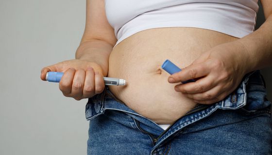 Eine übergewichtige Frau spritzt sich mit der Rechnet Hand ein Medikament in den Bauch.