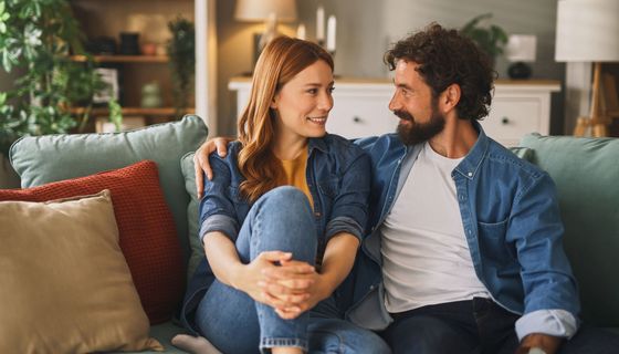 Ein Mann und eine Frau sitzen gemeinsam auf dem Sofa. Er hat seinen Arm um sie gelegt.
